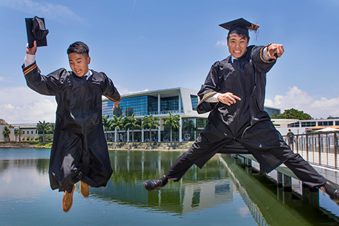 A couple of students celebrating graduation by jumping and posing