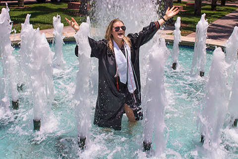 A student celebrates graduation by standing in a fountain